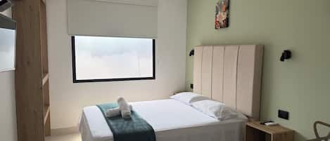 Un dormitorio con cama, ventana, una obra de arte en la pared y una mesita de noche.