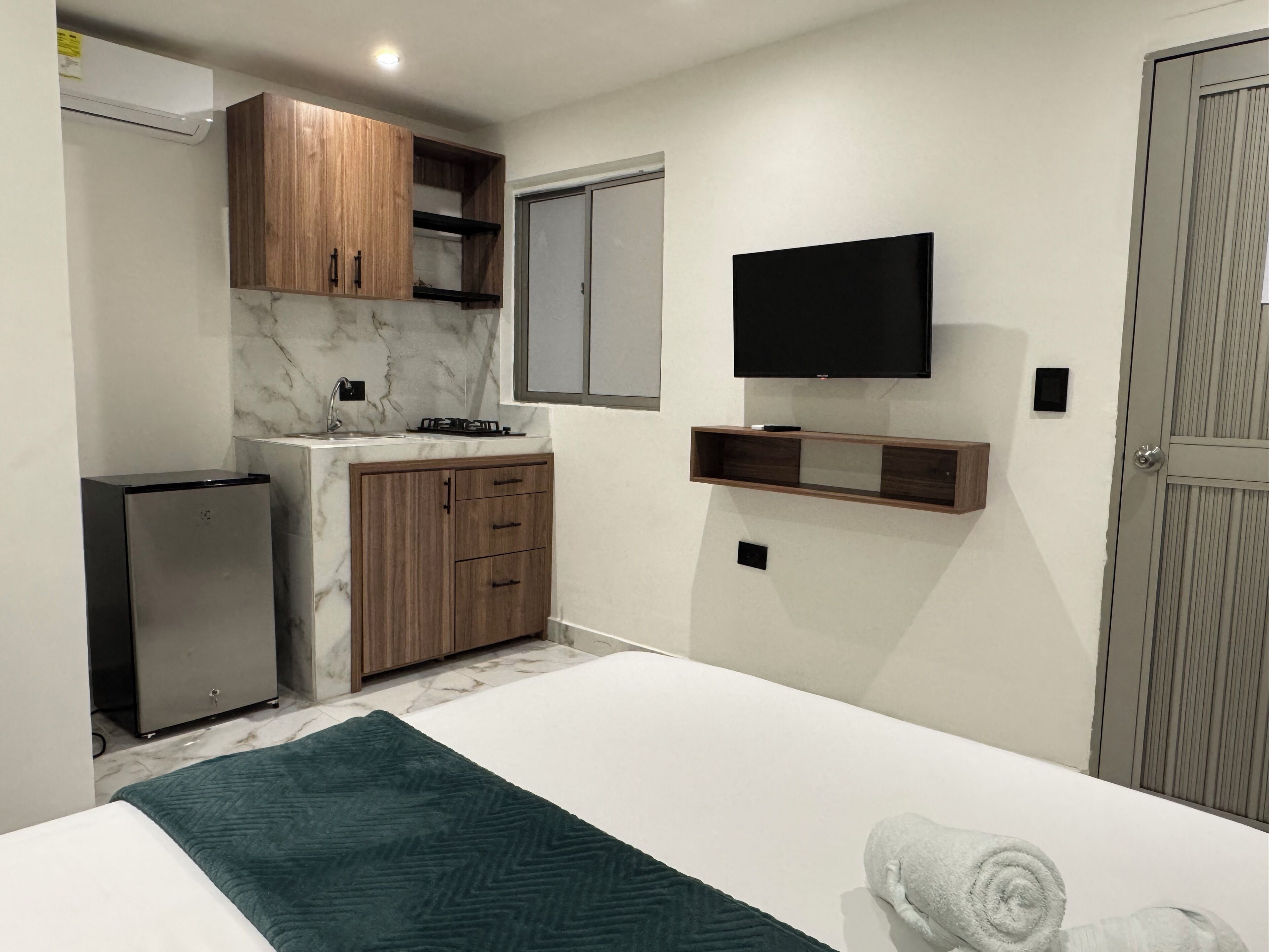 Une chambre d’hôtel compacte comprenant un lit, une petite kitchenette, un téléviseur fixé au mur et une armoire.