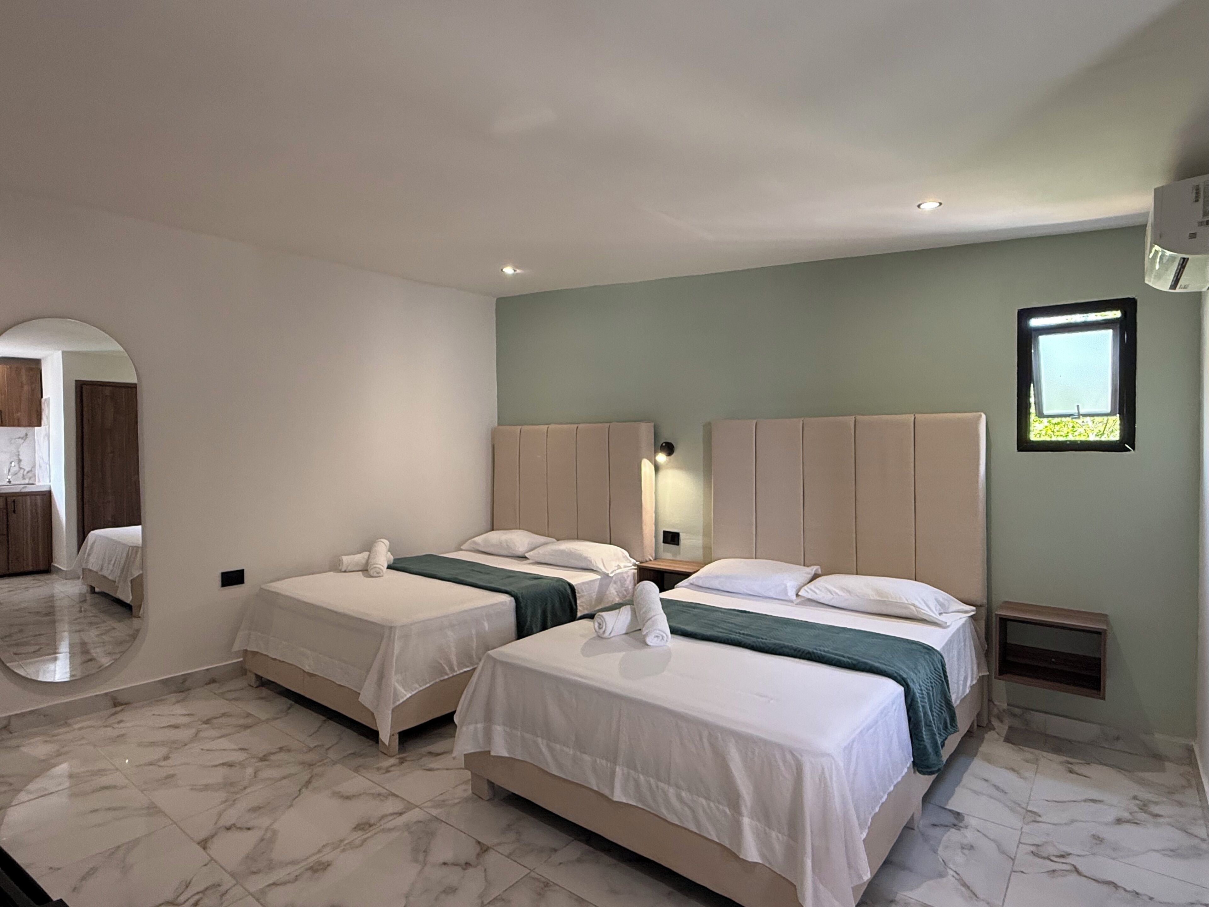 A hotel room with two beds, a small window, and a mirror.