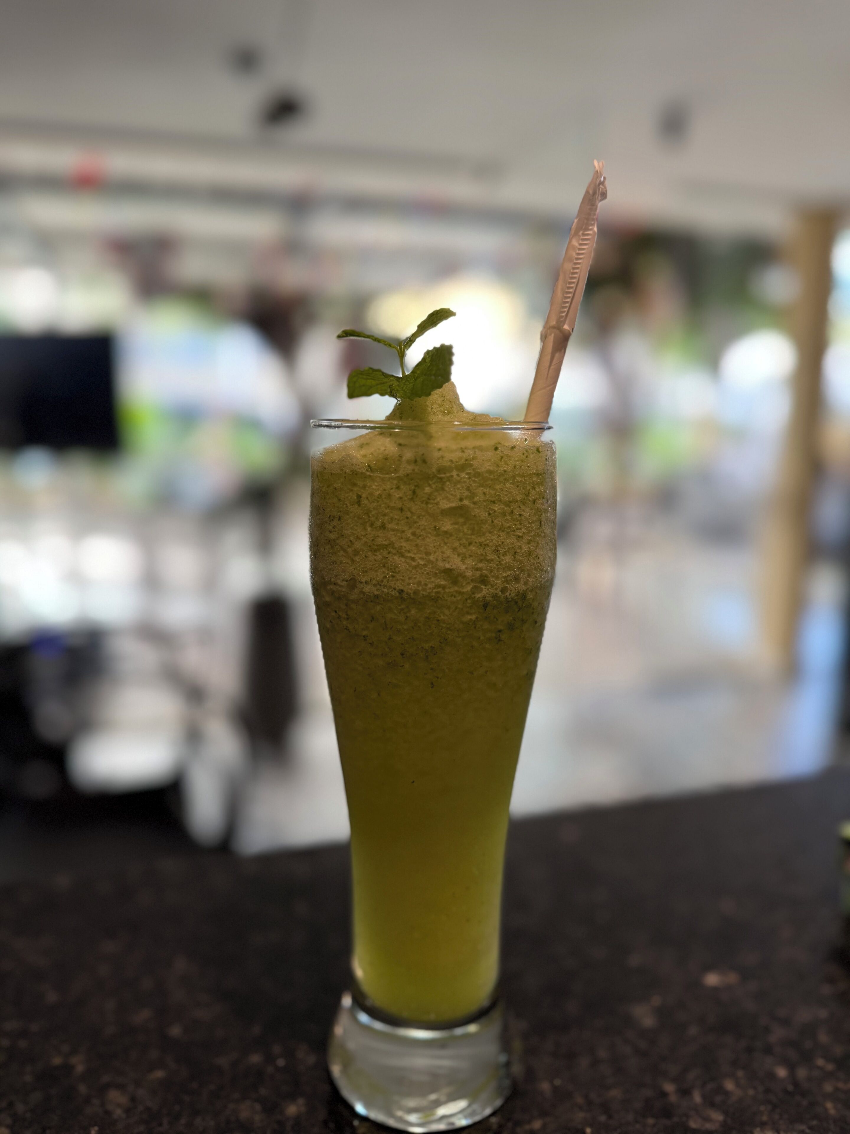 A tall glass with a green beverage, a mint leaf garnish, and a straw.