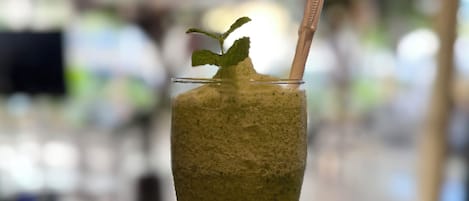A tall glass with a green beverage, a mint leaf garnish, and a straw.