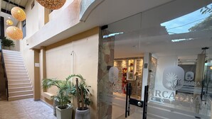 Entrada de hotel con puerta de vidrio, plantas en macetas y una escalera que lleva a un nivel superior.