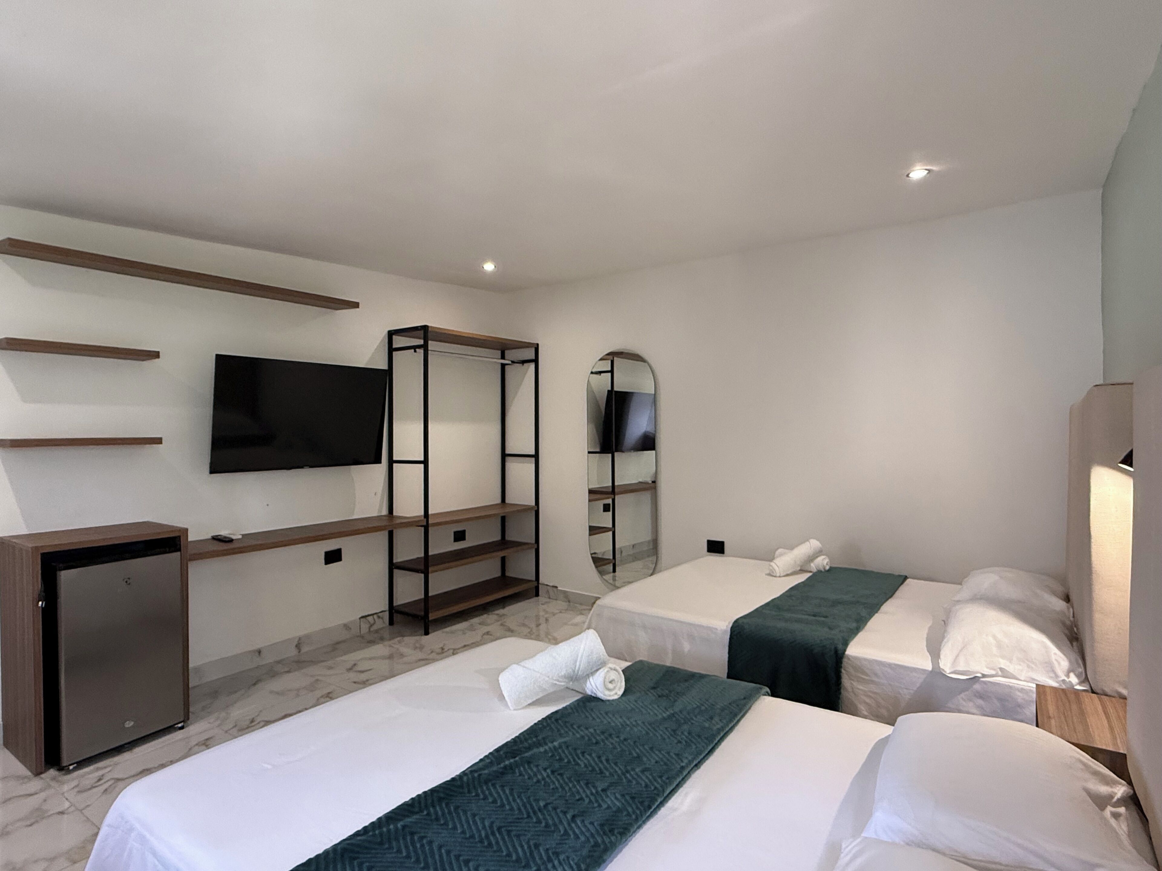 A hotel room with two beds, a desk, a television, and a mirror.