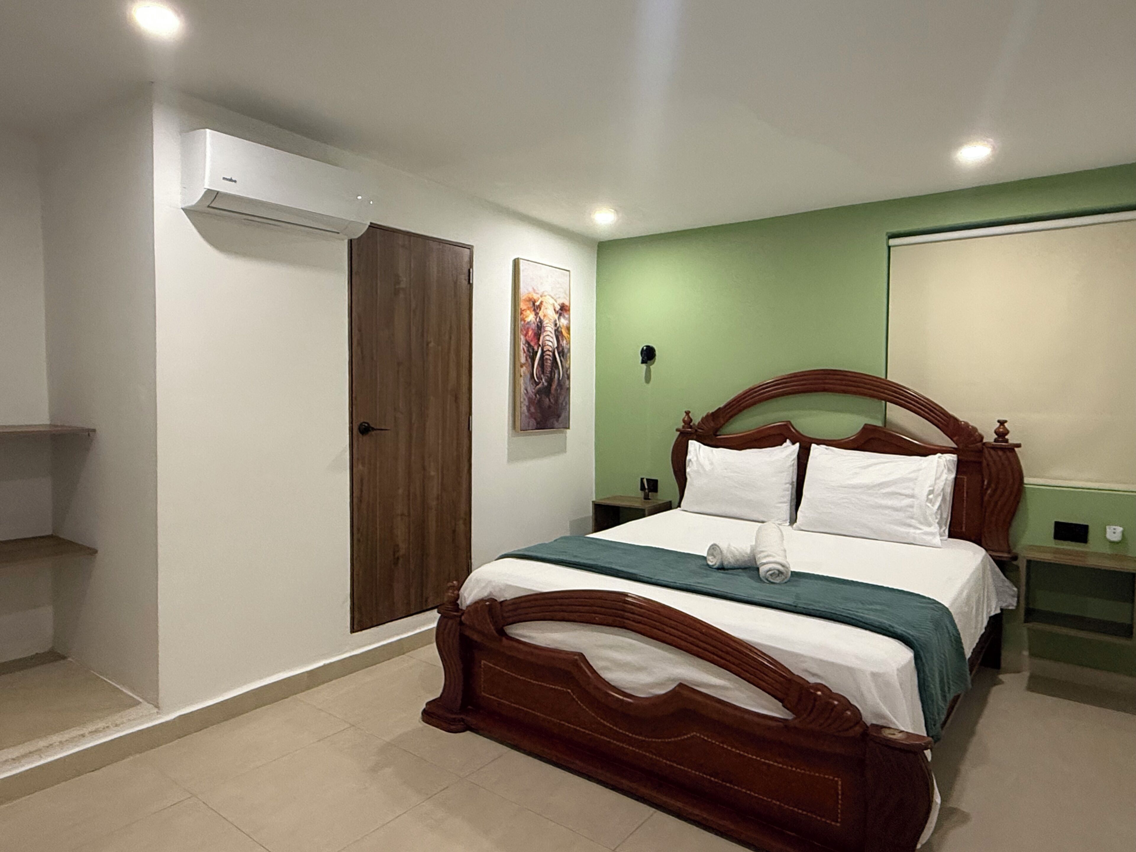 A bedroom with a wooden bed, a green wall, a door, and a wall-mounted air conditioner.