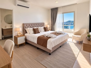 A hotel room with a bed, bedside tables, a desk, a chair, a TV, and a view of the city.