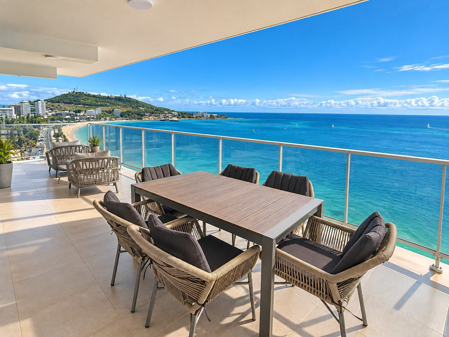 A balcony with a view of the sea, wicker furniture, and a table.