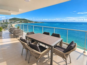 A balcony with a view of the sea, wicker furniture, and a table.