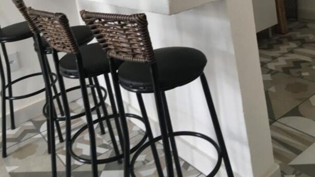 A kitchen with a tiled backsplash, a white countertop, and a built-in sink. There are four bar stools with woven seats and black metal frames. - Casinhas da Toca 1 - Quiet house 30 minutes from the main tourist attractions. (Armação dos Búzios)