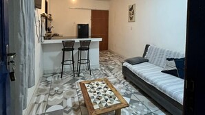 A compact living space with a kitchenette, a dining area with two bar stools, a sofa, and a patterned floor. - Casinhas da Toca 1 - Quiet house 30 minutes from the main tourist attractions. (Armação dos Búzios)
