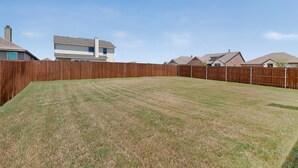 A fenced backyard with a grassy lawn, surrounded by houses. - Modern Home on the Texas Prairie (Gainesville)