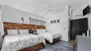 A modern bedroom with two beds, a ceiling fan, a flat-screen TV, and a dark door. - Beautiful Room Villa San Juan (Nuevo Vallarta)