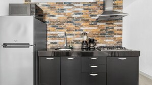 Una cocina compacta con un refrigerador de acero inoxidable, un microondas, una estufa a gas y un salpicadero de ladrillo.