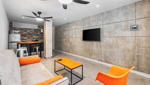 Una sala de estar moderna con un sofá, sillas anaranjadas, una mesa de centro y un televisor montado en la pared.