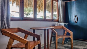 Een kamer met twee houten stoelen en een kleine tafel, een donkerblauwe kast, en een raam met uitzicht op bomen en een gebouw.