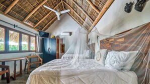 Een kamer met een bed, overdekt met witte lakens, een houten hoofdbord, een klamboe en een plafondventilator.