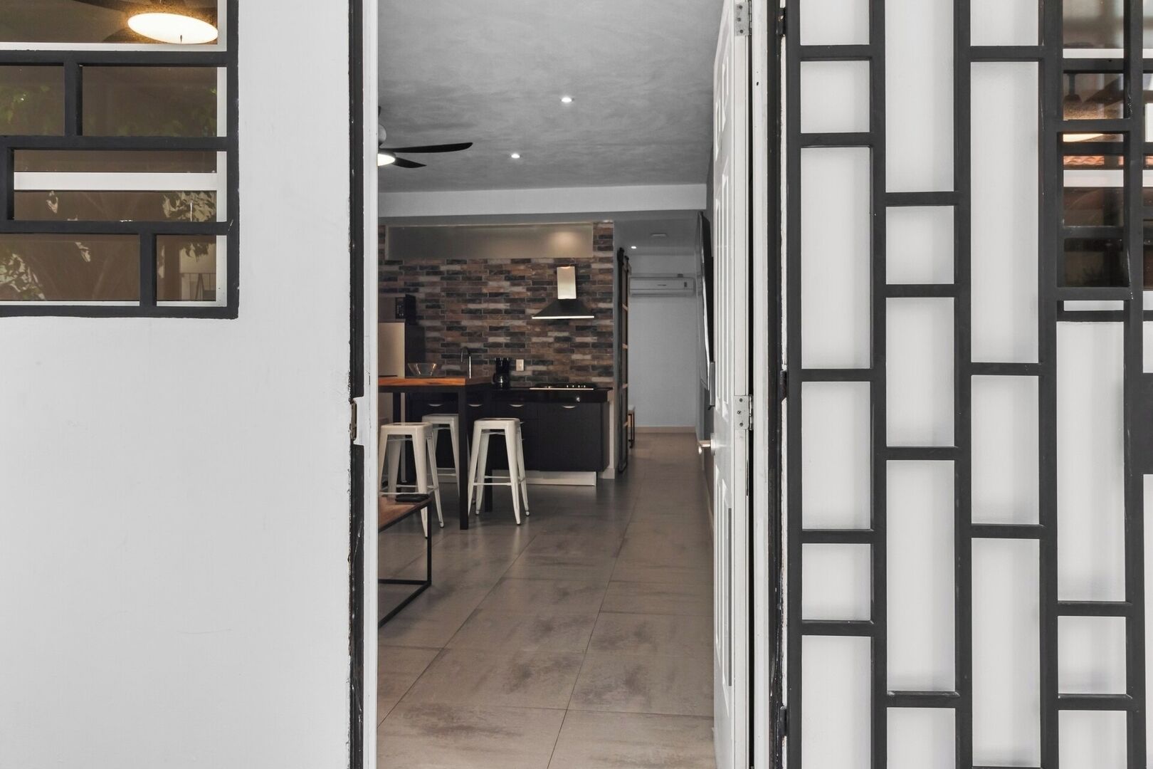 Vista del interior de una cocina moderna con salpicadero de ladrillo, una isla central con taburetes y un ventilador de techo.