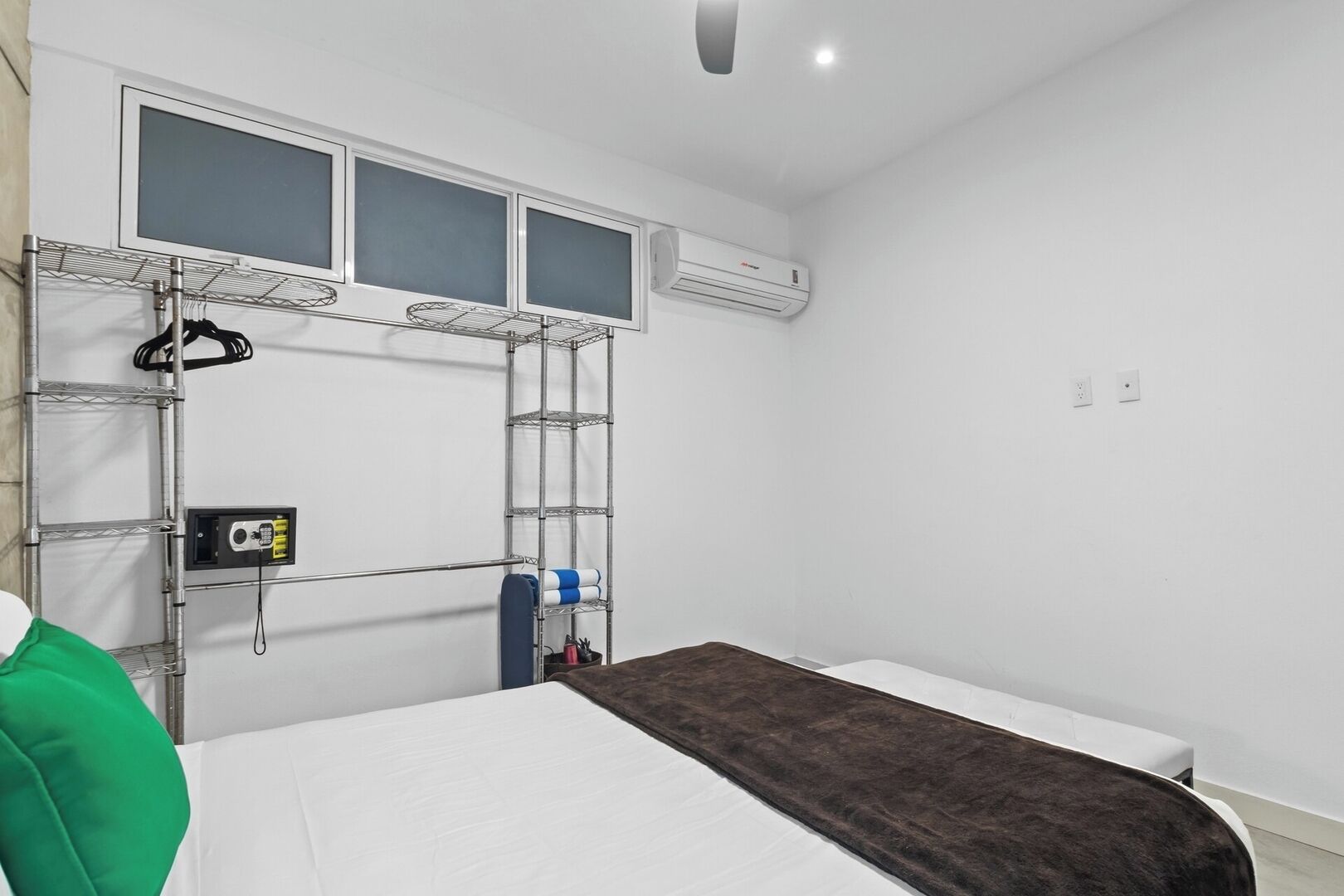 Une chambre avec un lit superposé, un lit blanc, une couverture marron, une étagère en métal et un appareil de climatisation.