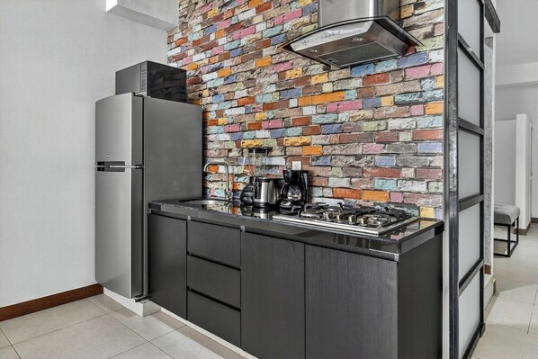 A compact kitchen with a modern stainless steel refrigerator, a gas stove, and a coffee maker.