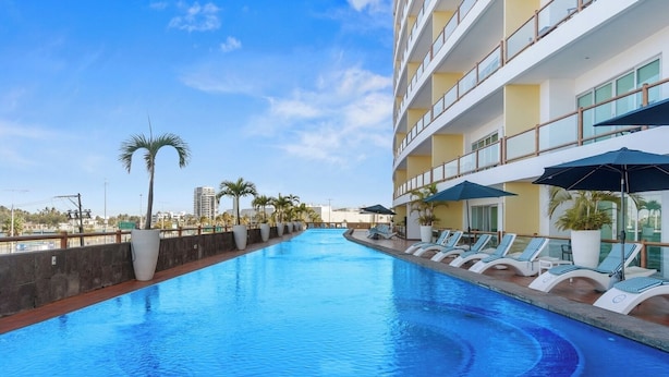 Une piscine entourée d’un bâtiment doté de balcons, avec des chaises longues et des parasols à proximité.