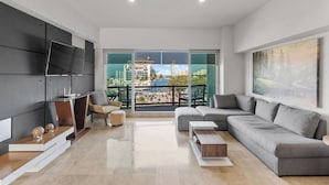 Un salon moderne avec un canapé gris, un téléviseur fixé au mur et un balcon offrant une vue sur la ville.