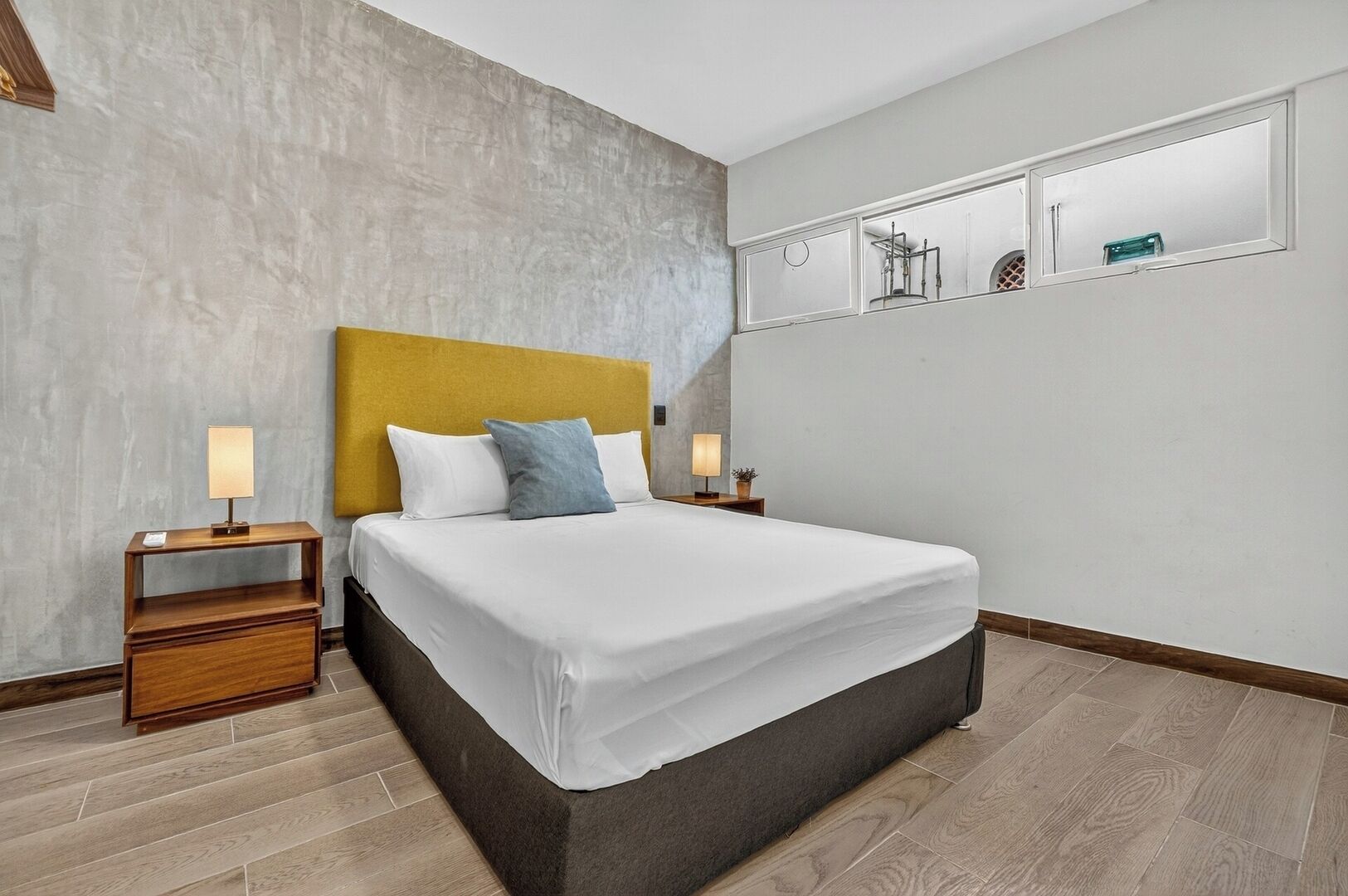A modern hotel room with a large bed, wooden nightstands, and a grey concrete wall.