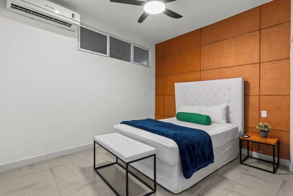 Un dormitorio moderno con una cama, un banco, una mesita de noche y un ventilador de techo.