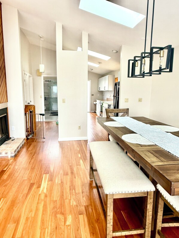 A modern kitchen with wooden flooring, a dining area with a long table and benches, and a skylight above.