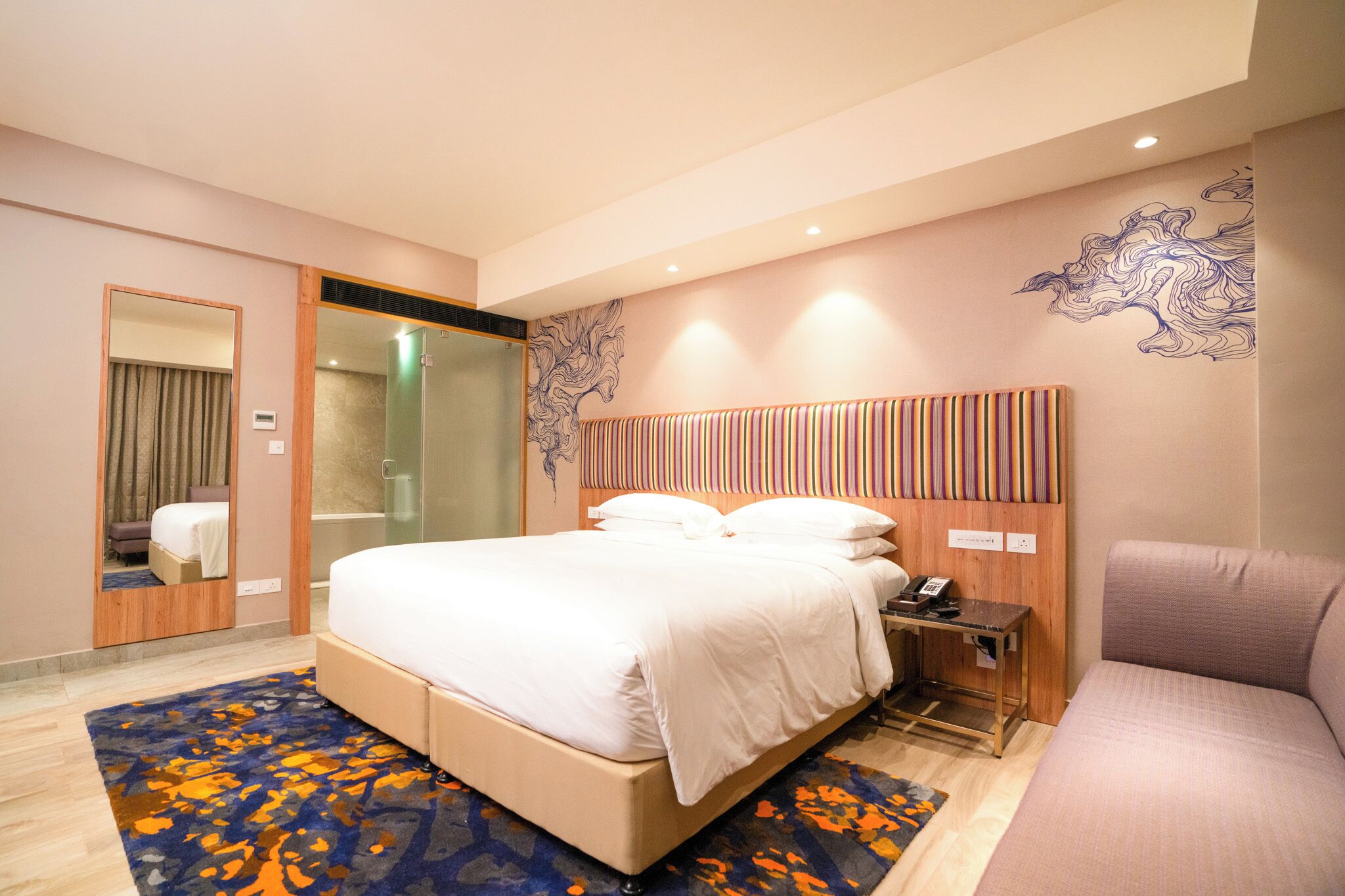 Habitación de hotel con cama, mesita de noche con teléfono, zona de ducha y un espejo grande.