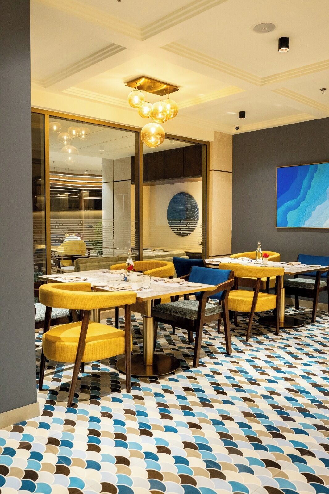 A modern dining area with yellow chairs, round tables, and a patterned floor.