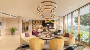 A spacious lobby with a modern chandelier, comfortable seating, a central coffee table, and large windows offering a view. - Vivanta Kochi Aluva (Aluva)