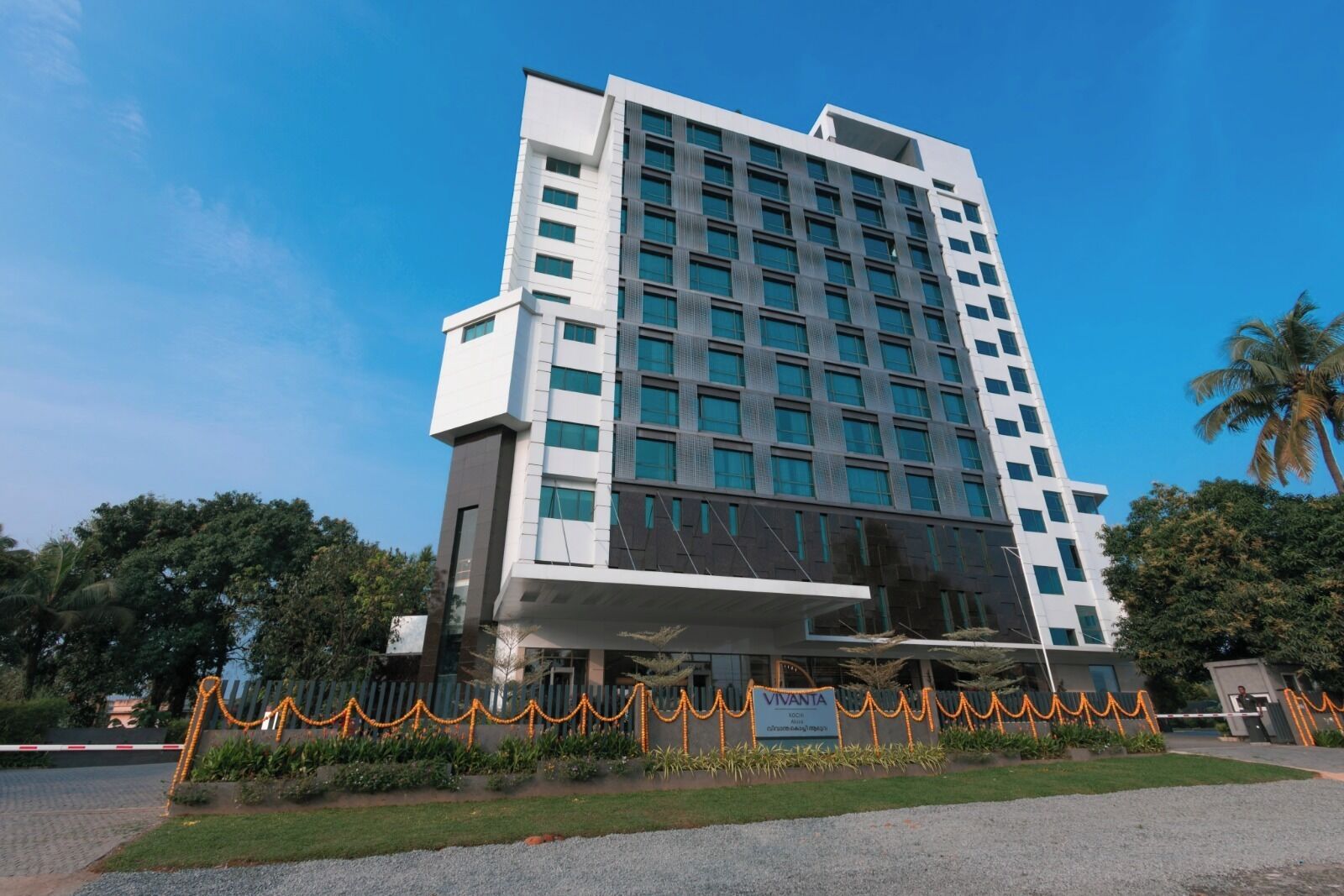 Un hotel moderno de varios pisos con una entrada destacada, un letrero y un área ajardinada.