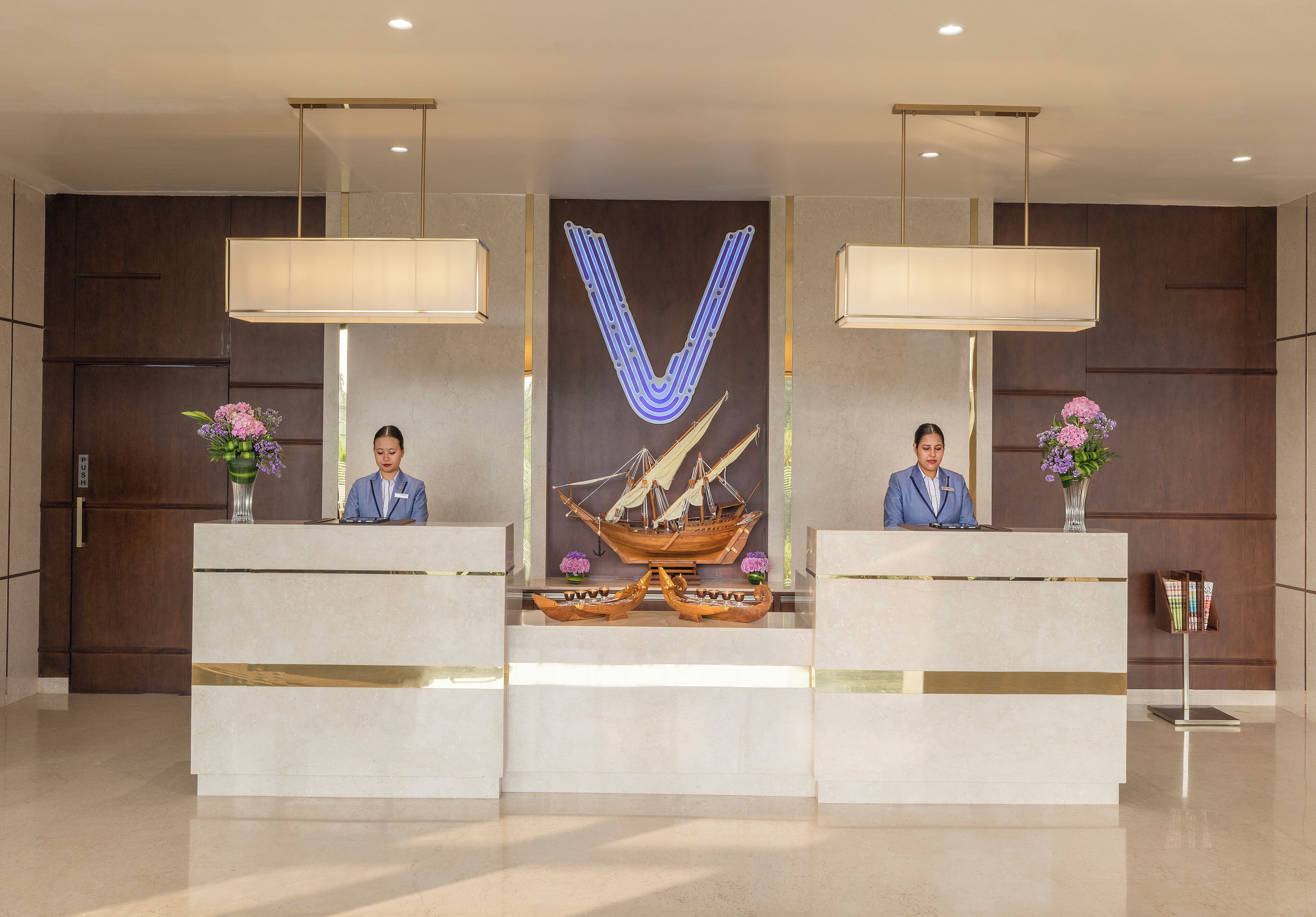 A reception area with two receptionists, a large V-shaped light fixture, and a decorative ship model.