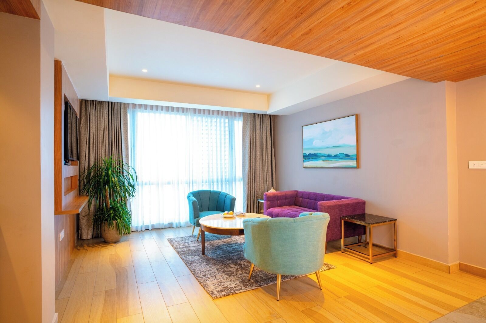 Una sala de estar moderna con techo de madera, un ventanal con cortinas, un sillón azul, un sofá morado y un cuadro en la pared.