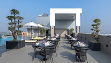 A rooftop terrace with outdoor seating, a pool, and a modern building structure.