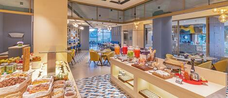 Buffet-alue, jossa on tarjolla monenlaista ruokaa, sekä ruokailualue, jossa on pöytiä ja tuoleja.