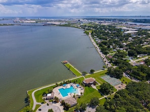 An aerial view of a residential area with a large body of water, a dock, and a swimming pool.
