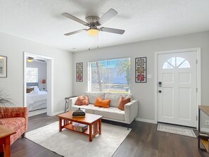 A living room with a white sofa, a coffee table, a ceiling fan, and a door with a welcome mat.