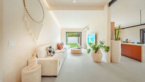 Una sala de estar moderna con sofá, mesa de centro y objetos decorativos. Hay una zona de cocina con mostrador y armarios.