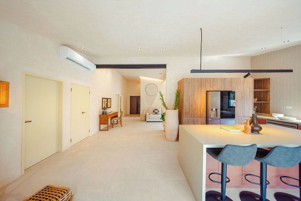 A modern kitchen with wooden cabinets, a central island with bar stools, and a dining area with a sofa and coffee table.