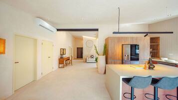A modern kitchen with wooden cabinets, a central island with bar stools, and a dining area with a sofa and coffee table.