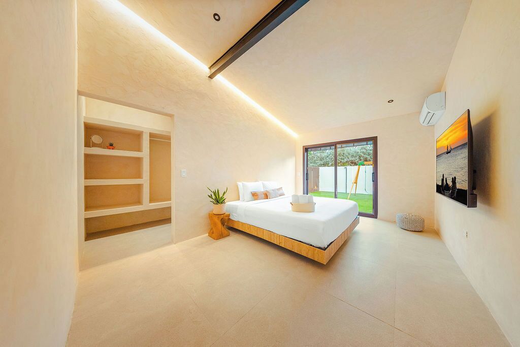 A modern bedroom with a bed, built-in shelving, a potted plant, and a large window.
