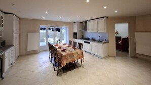 Una cocina amplia con armarios blancos, una mesa de comedor para cuatro personas y vistas a un área exterior a través de un ventanal.