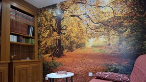 Una habitación con una estantería, una mesa redonda con superficie blanca y un sofá estampado con hojas.