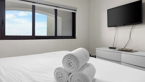 Una habitación de hotel con un ventanal grande, un televisor de pantalla plana montado en la pared y una cama bien hecha con toallas blancas enrolladas.