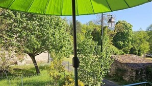 Uma varanda com um guarda-sol verde, uma cadeira e vista para árvores e um muro de pedra.