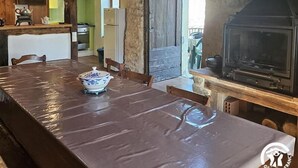 Uma área de refeições rústica com uma mesa comprida, vigas de madeira e uma parede de pedra.