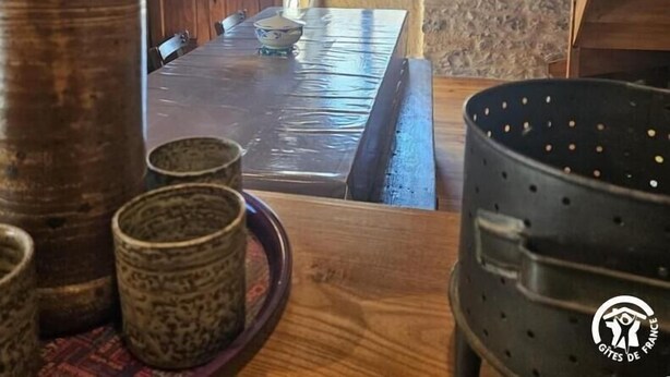 Interior rústico de pedra com uma mesa de jantar de madeira, bancos e uma panela grande.