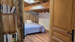 Quarto rústico com teto de madeira, parede de pedra e cama com colcha acolchoada.