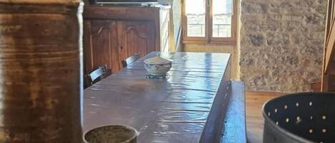 Interior rústico de piedra con una mesa de madera, bancos y una olla grande.