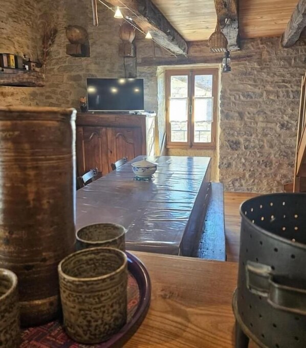 Un intérieur rustique en pierre, avec une table à manger en bois, des bancs et un grand pot.